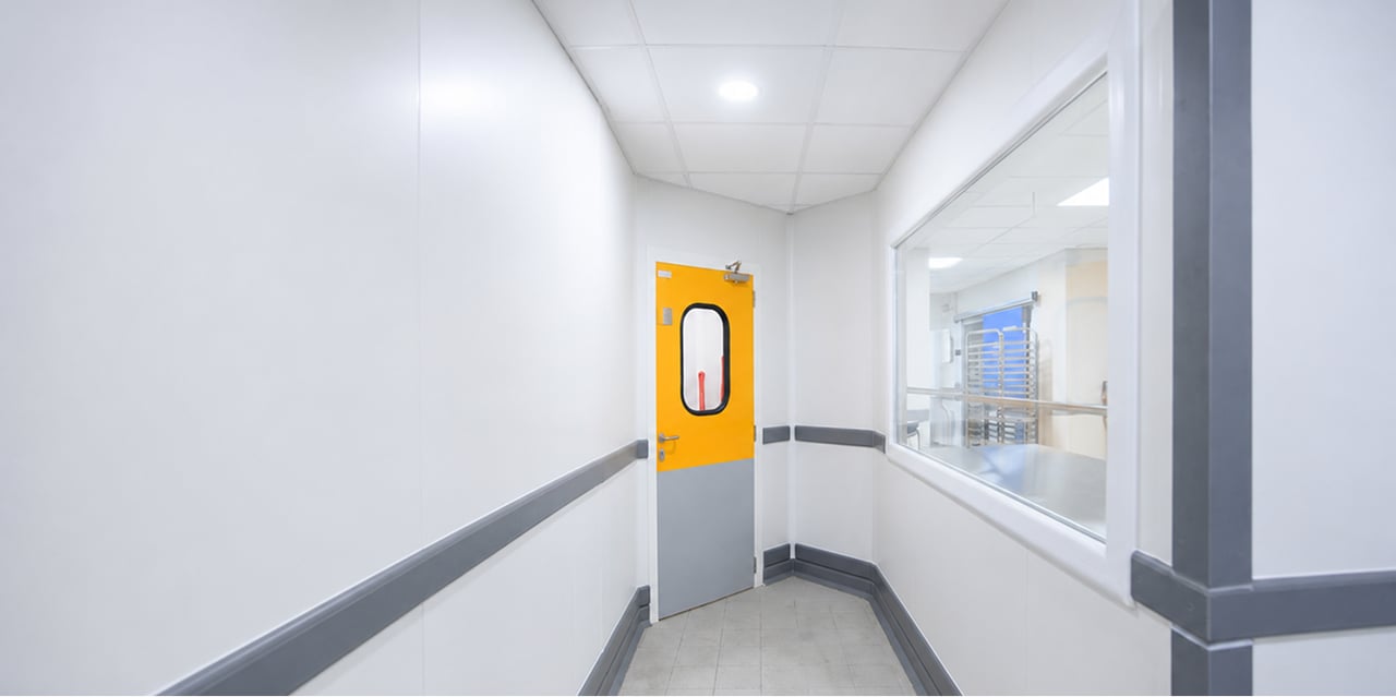 Corridor with a yellow swing door and a glazed window onto a ward